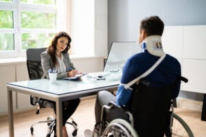 A truck accident victim in a wheelchair with a neck brace and an arm sling discussing his case with an experienced truck accident lawyer in Watertown.