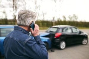 Man calling his auto insurance company while standing in front of two cars involved in an auto collision and wondering what the statute of limitations for a car accident claim in South Dakota is.